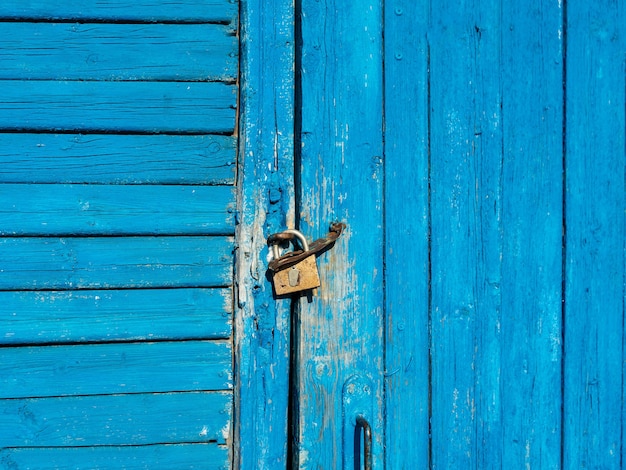 La porta di legno con vernice blu scrostata è chiusa con un lucchetto.