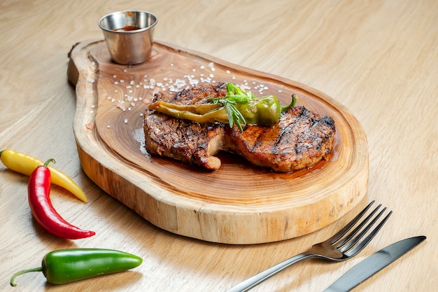 La porzione ha grigliato la bistecca di New York con salsa, pomodoro sul bordo di legno. Servizio al ristorante.