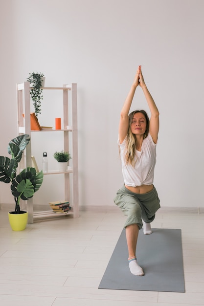 La pratica dello yoga della donna esegue la posa sul tappetino all'interno di una stanza accogliente con piante e vegetazione sana