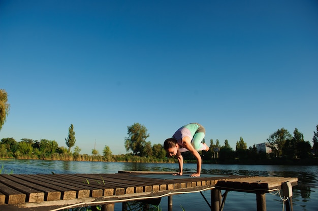 La pratica equilibrata di stile di vita sano della donna medita ed energia lo yoga sul ponte nella mattina la natura.