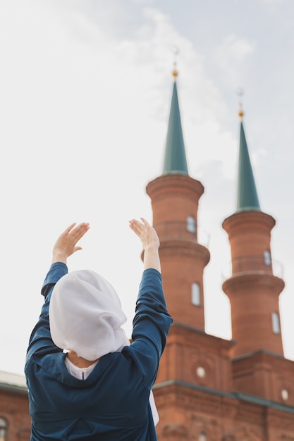 La preghiera della donna musulmana indossa l'hijab il digiuno prega ad Allah sullo sfondo della moschea