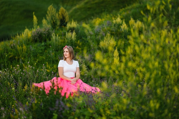La principessa in un abito rosa estivo si siede sull'erba verde La ragazza in un campo di fiori in un paese