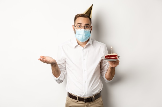 La quarantena del coronavirus e le vacanze hanno confuso l'uomo con la maschera facciale che tiene la torta di compleanno e scrolla le spalle...