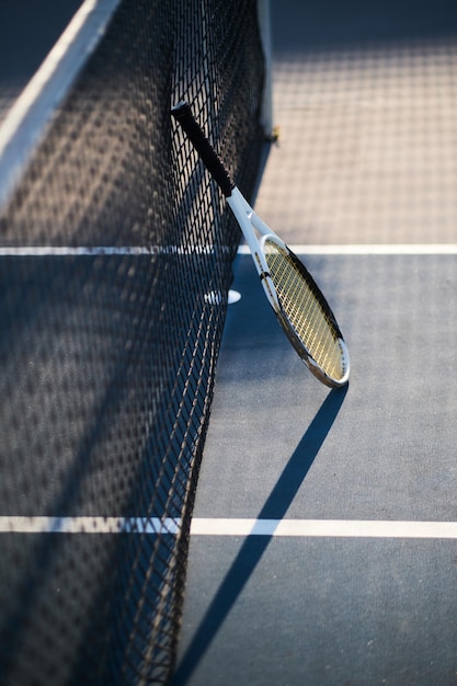 La racchetta da tennis è in piedi vicino alla rete da tennis all'esterno in una luminosa giornata di sole.