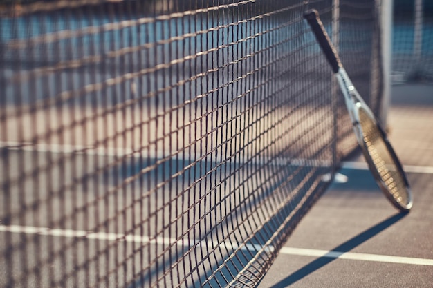 La racchetta da tennis è in piedi vicino alla rete da tennis all'esterno in una luminosa giornata di sole.