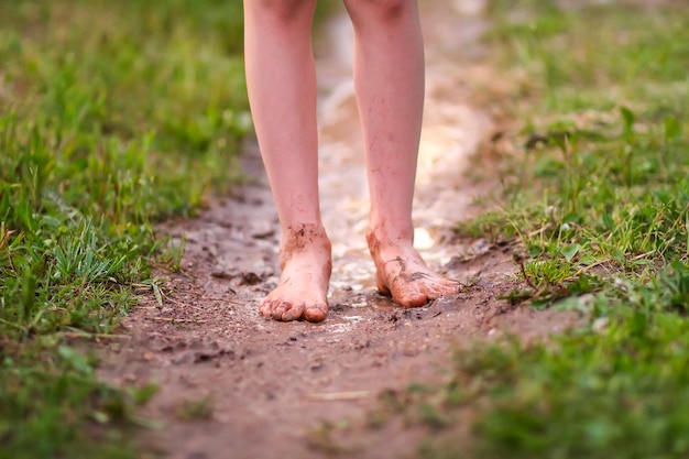 La ragazza a piedi nudi cammina attraverso pozzanghere d'acqua dopo la pioggia estiva in campagna.