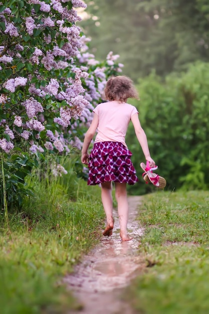 La ragazza a piedi nudi cammina attraverso pozzanghere d'acqua dopo la pioggia estiva in campagna.