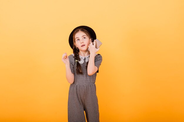 La ragazza abbastanza sorridente sta tenendo lo smartphone. Bambino carino su sfondo giallo, concetto di bambini moderni.