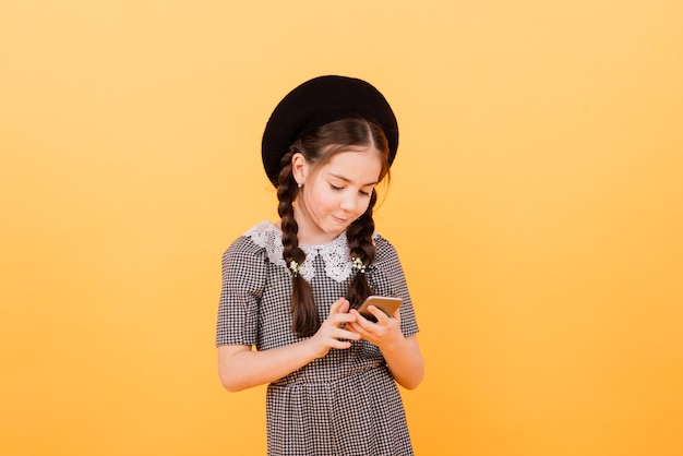 La ragazza abbastanza sorridente sta tenendo lo smartphone. Bambino carino su sfondo giallo, concetto di bambini moderni.