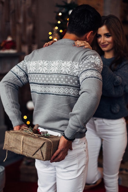 La ragazza abbraccia il ragazzo e lo guarda ragazzo con in mano la sorpresa del regalo di Natale per la vista posteriore della ragazza