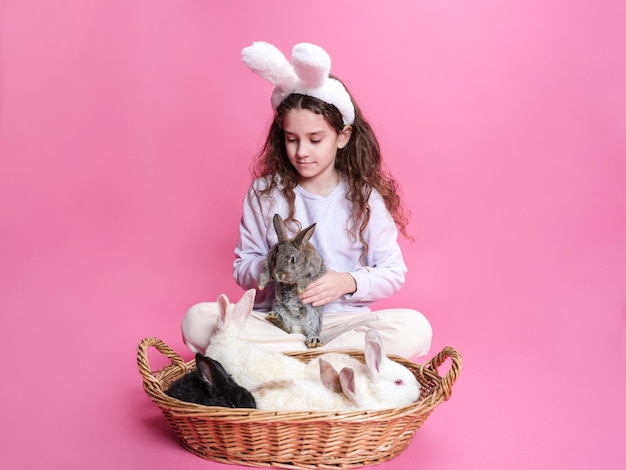 La ragazza abbraccia un simpatico coniglio grigio in studio isolato sfondo rosa ha diversi conigli di animali domestici in un cestino