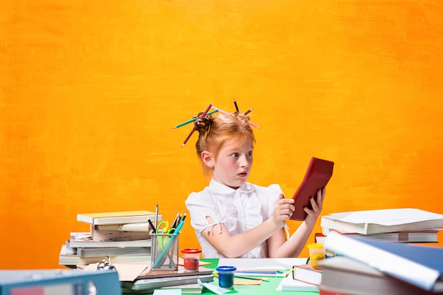 La ragazza adolescente dai capelli rossi con molti libri a casa. Foto in studio