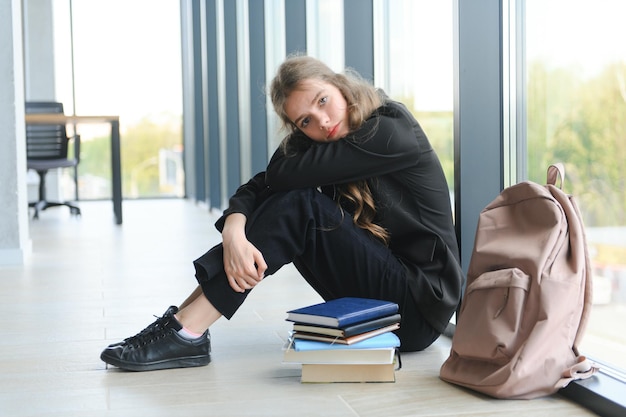 La ragazza adolescente sconvolta si siede sul pavimento guardando tristemente fuori dalla finestra preoccupata per il problema adolescenziale a scuola e la comunicazione con i genitori La ragazza preoccupata soffre tesa per il bullismo a scuola amore non corrisposto con il ragazzo