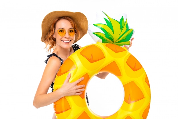 La ragazza adorabile in un cappello di paglia con un ananas ha modellato il cerchio di nuoto su bianco