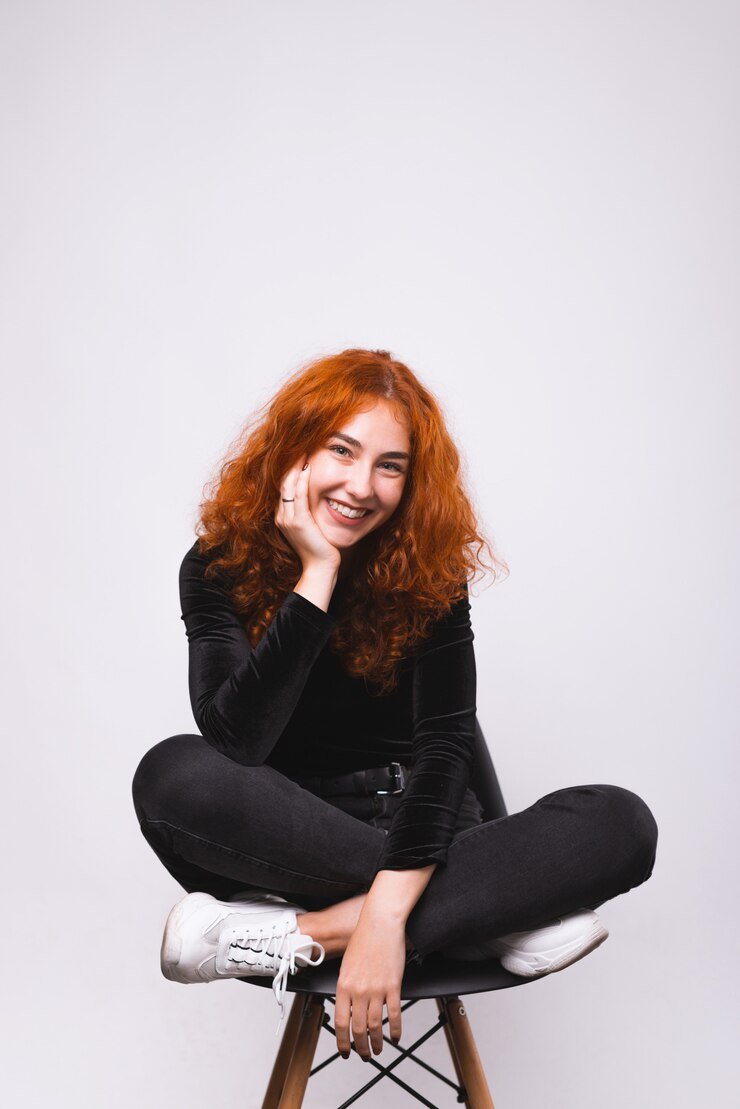 Foto la ragazza adorabile sta sedendosi sulla sedia e sta sorridendo vicino alla carta da parati bianca.