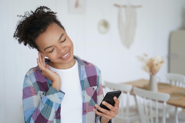 La ragazza afroamericana ascolta la musica utilizzando lo smartphone a casa Pubblicità di app musicali