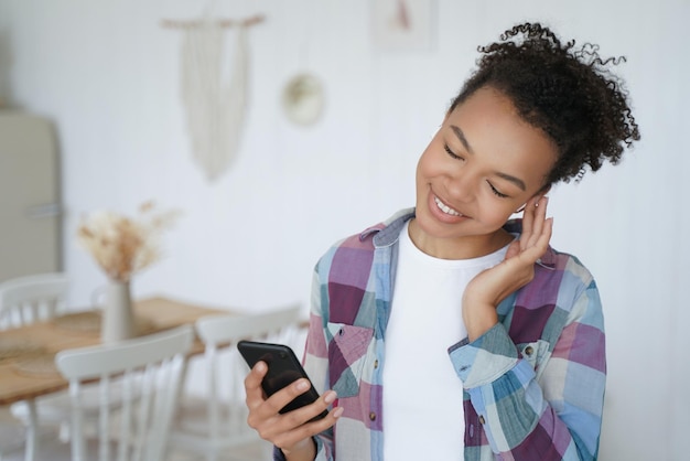 La ragazza afroamericana ascolta la musica utilizzando lo smartphone a casa Pubblicità di app musicali