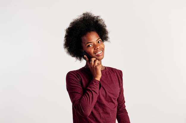 La ragazza afroamericana in maglione marrone posa mentre parla al telefono.