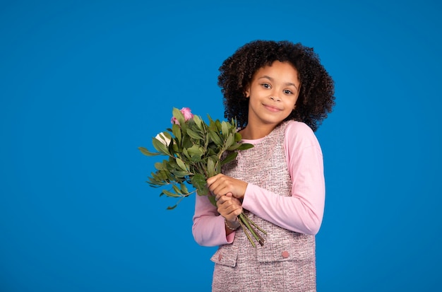 La ragazza afroamericana teenager felice con il mazzo dei fiori che celebra la festa gode della primavera