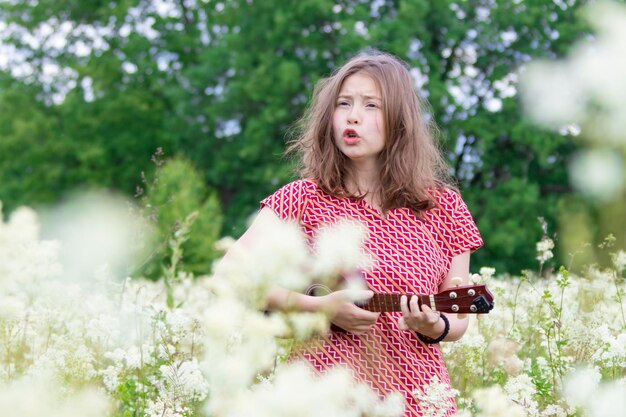 La ragazza al mattino presto cammina sul prato con l'ukulele