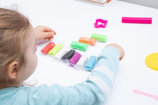 La ragazza al tavolo sta giocando con la pasta da modellare. Giochi per bambini per la motricità fine