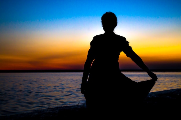 La ragazza al tramonto sta sulla riva e guarda lontano in attesa di un miracolo