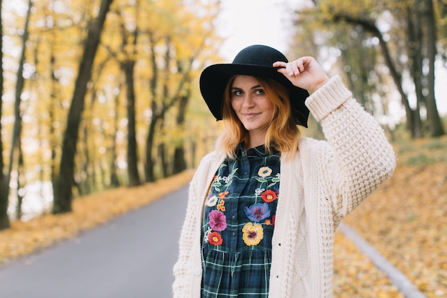 La ragazza alla moda di hippy in un maglione e un cappello tricottati cammina nel parco di autunno.