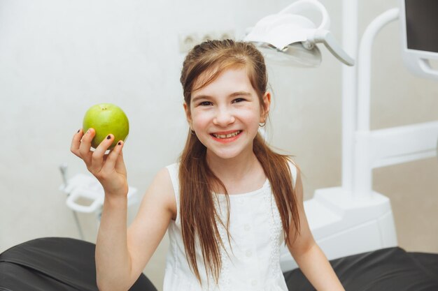 La ragazza alla reception del dentista pediatrico sorride e ride una bambina tiene una grande mela verde nelle sue mani concetto di salute dei bambini