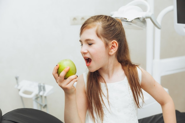 La ragazza alla reception del dentista pediatrico sorride e ride una bambina tiene una grande mela verde nelle sue mani concetto di salute dei bambini