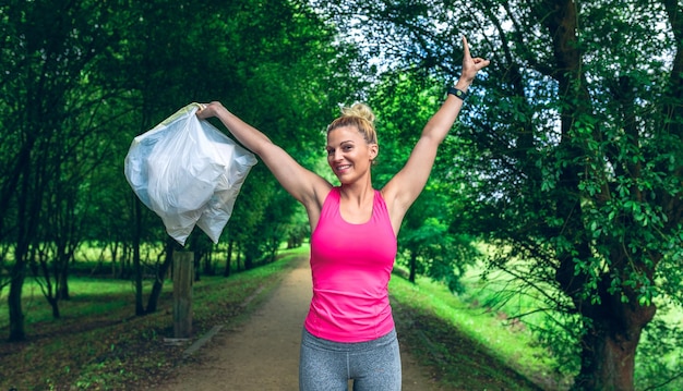 La ragazza alza le braccia mostrando i sacchi della spazzatura facendo plogging