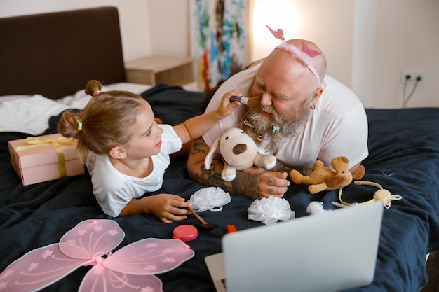 La ragazza applica la polvere sulla faccia di papà guardando video tramite laptop a casa