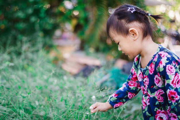 La ragazza asiatica adorabile gode di con erba e fiore in giardino all&#39;aperto