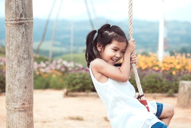 La ragazza asiatica felice del piccolo bambino che si diverte a giocare su di legno oscilla nel campo da giuoco al giardino