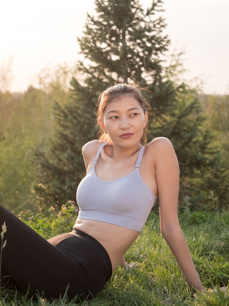 La ragazza asiatica in abiti sportivi si siede con un sorriso sull'erba.