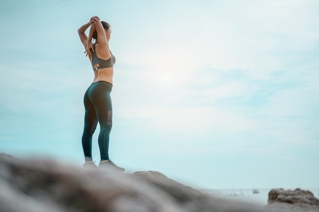 La ragazza asiatica si esercita durante gli esercizi del fine settimana e allunga il suo corpo sulla spiaggia in buona salute