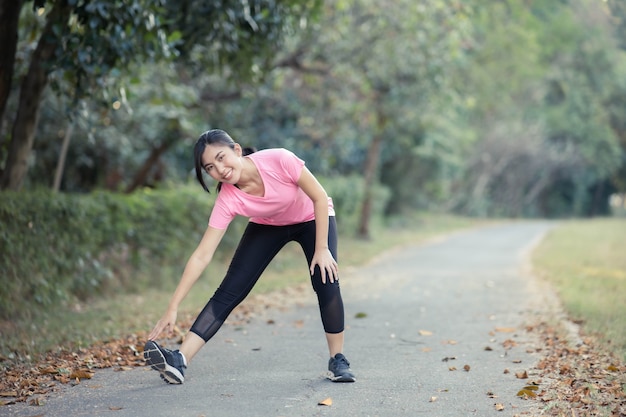 La ragazza asiatica sta allungando i muscoli caldi del suo corpo prima di uscire per una corsa al parco