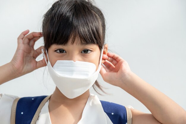 La ragazza asiatica sullo sfondo bianco indossa una maschera facciale che protegge dalla diffusione del coronavirus