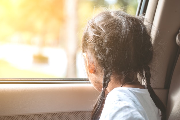 La ragazza asiatica sveglia del piccolo bambino che si siede nell&#39;automobile e guarda fuori dal finestrino di automobile nel tramonto