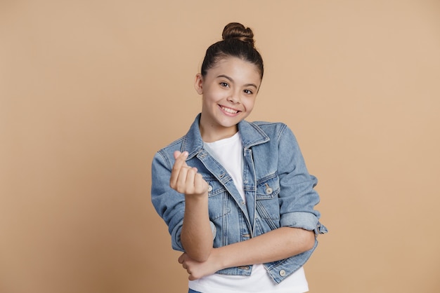 La ragazza astuta e sorridente mostra un segno di soldi. Ragazza che gesticola su uno sfondo marrone