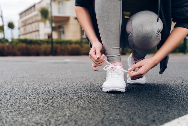 La ragazza atletica lega i lacci delle scarpe sulle scarpe da ginnastica su un campo sportivo all'aperto