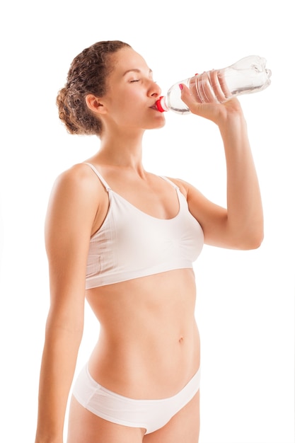 La ragazza atletica sottile beve l'acqua da una bottiglia isolata su bianco.