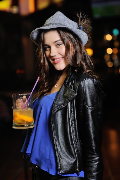 La ragazza attraente in un cappello bavarese grigio beve la birra o un cocktail della birra attraverso una cannuccia di un ba