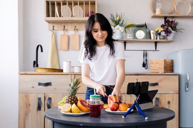 La ragazza attraente prepara i frullati di frutta