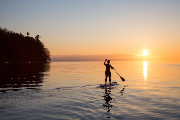 La ragazza avventurosa su una tavola da paddle sta remando durante un tramonto luminoso e vibrante