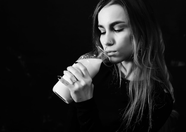 La ragazza beve il latte da una bottiglia su un fondo nero della parete