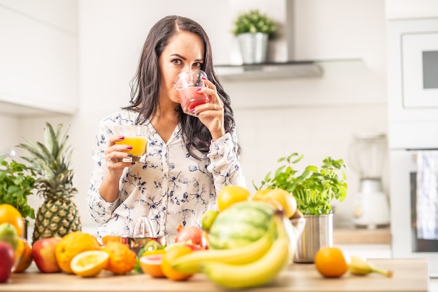 La ragazza beve succo di frutta fresco a casa con altri tipi di frutta sulla scrivania della cucina di fronte a lei.