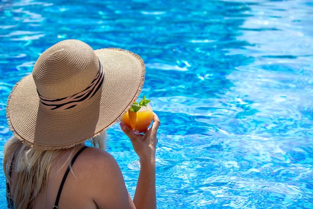 La ragazza beve un cocktail nel fuoco selettivo della piscina