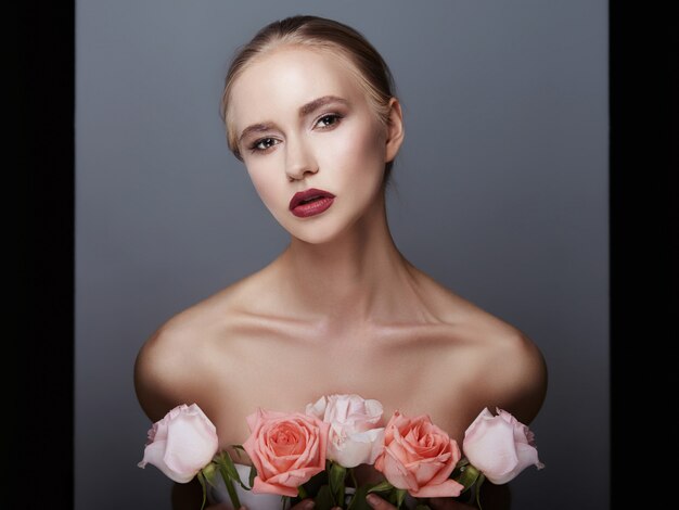 La ragazza bionda che tiene i fiori rosa si avvicina al fronte. bellezza