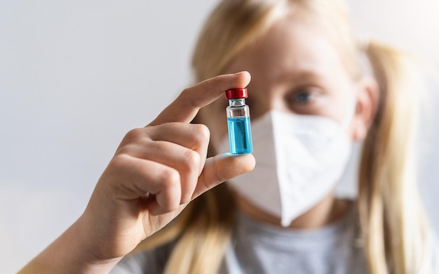 la ragazza bionda con maschera facciale mostra un flacone di vaccino con veleno blu per il vaccino Covid-19 in un centro di vaccinazione.