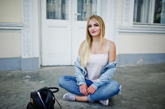 La ragazza bionda indossa i jeans con lo zaino in posa contro la vecchia porta